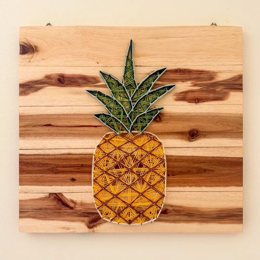 String-art pineapple mounted on a reclaimed pallet-wood backdrop