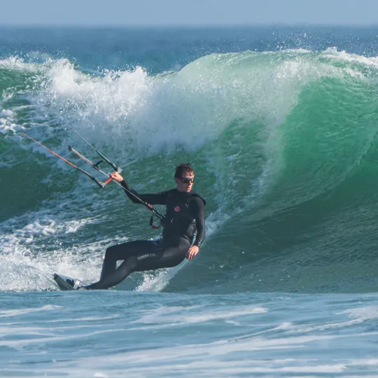 Lars kitesurfing across the face of a green wave