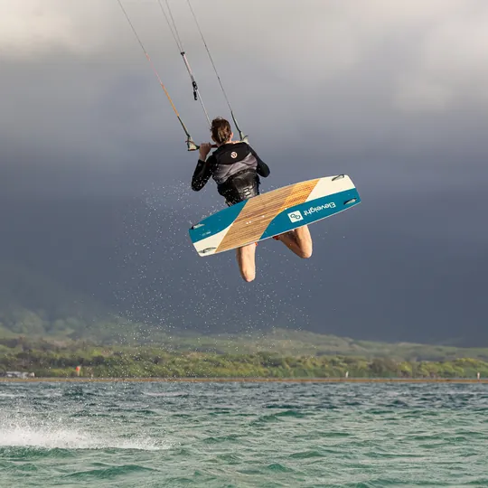 Lars boosting a kitesurf jump with a board grab, mountains behind
